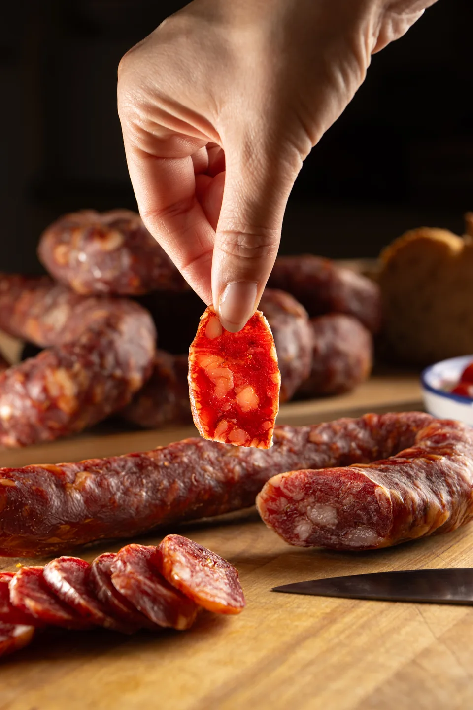 Una mano solleva una fetta di lucanica sopra il tagliere.